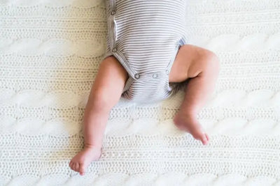 A baby girl lies in a crib with her American made, organic bodysuit.