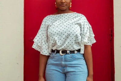 A woman standing in front of a red door wears a white and black blouse that was made in America. 