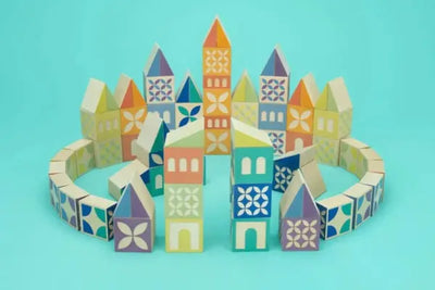 Colorful wooden blocks arranged as a miniature cityscape on a turquoise background. Features vibrant towers, geometric patterns, and a circular wall, creating a playful and artistic scene.