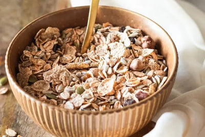 A brown bowl and spoon with granola in it.