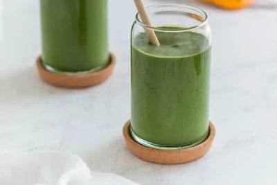 Two glasses with green matcha sit on table coasters.