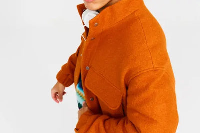 A man wearing an orange American-made jacket with white headphone around his neck.