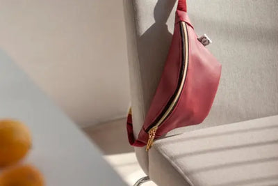 A pink leather fanny pack that was made with USA leather is draped over a chair. 