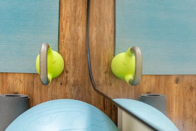 A blue exercise ball, two green kettlebells, and yoga mats reflected in a mirror.