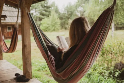 A person sitting in a colorful hammock, reading a book outdoors in nature.