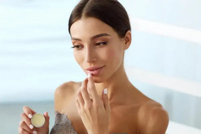 A women holding lip balm in her hand puts organic lip balm on her lip. 