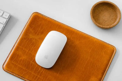 A mouse sitting on a leather mousepad.