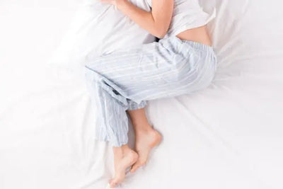 American made white pajama bottoms being worn by a women sitting in bed. 