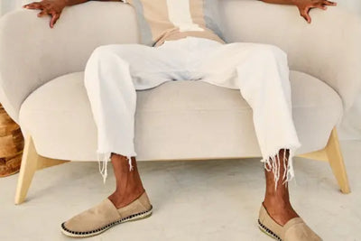 A man sitting on a beige chair is wearing white, American-made pants.