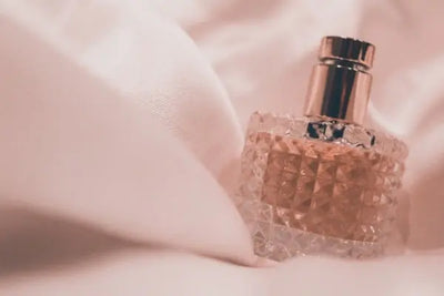 Pink perfume spray bottle sitting on a blanket cover. The perfume was designed and manufactured in the United States of America. 