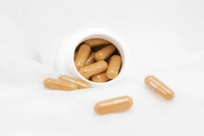Open bottle of American made vitamins and supplements sit on a counter with pills sitting around the bottle.