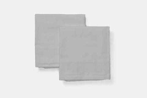 Two neatly folded, light gray Natural Cotton Bed Pillowcases by American Blossom Linens, featuring a simple, smooth texture and luxurious fabric, are placed side by side on a plain white background.