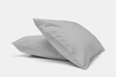 Two plain white pillows with American Blossom Linens Natural Cotton Bed Pillowcases are stacked on a white surface, with one pillow slightly atop the other, set against a plain white background.