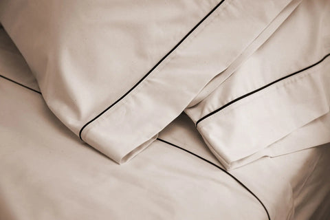 Close-up of American Blossom Linens Cotton Piping Design Bed Sheet Set, expertly crafted from USA-grown cotton in a luxurious cream color with thin black piping along the edges.
