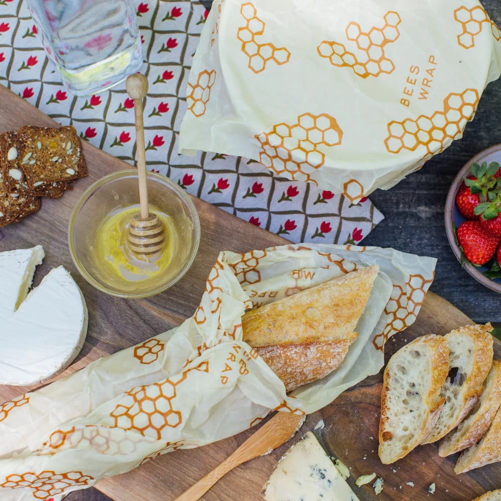 Beeswax wrap used to wrap bread and cheese on a table with honey and fruit.