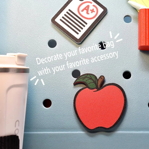 FRESHe Baglets by Chatelet Manufacturing: Apple Teacher Charms for tote bags are shown attached to a blue bag with holes. The text “Decorate your favorite bag with your favorite tote bag accessory” appears overhead, plus a white bottle on the left.