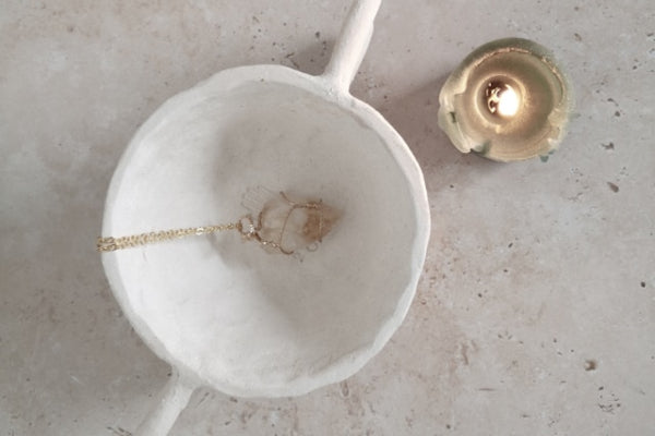 Gold necklace draped over a white marble dish on a light gray surface.
