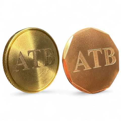 The Fairway Reserve Personalized Ball Markers (Set of 2) includes a brass-colored round marker and a copper-toned angular marker, both engraved with ATB on the front.