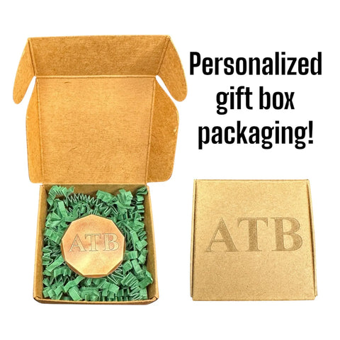 A brown Fairway Reserve gift box with ATB embossed on the lid, filled with green shredded paper and two personalized ball markers inside. Text beside the box reads: Personalized Ball Markers (Set of 2) in custom gift packaging!.