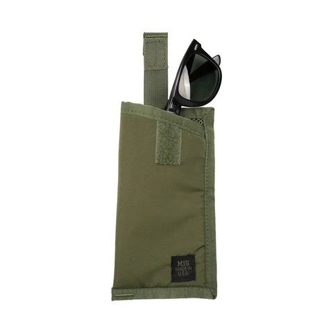A pair of black sunglasses partly tucked into an olive EW Soft Case by MIS, made of green nylon with a Velcro strap, tactical key strap, and a small black MIS MADE IN USA label on the bottom right corner.