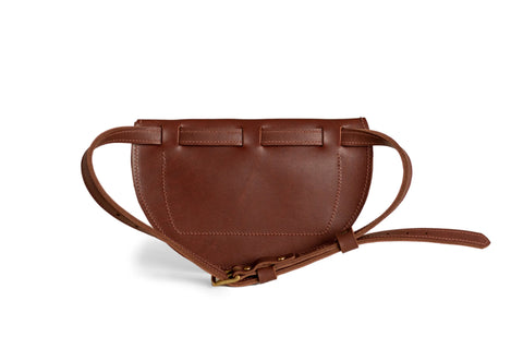 The Urban Southern Half-Moon Belt Bag is a handcrafted brown leather fanny pack made in the USA, showcasing a curved design, prominent stitching, rear belt loops, and an adjustable front strap. Shown against a white background.