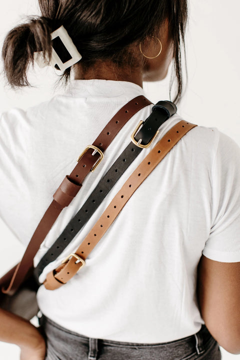A woman with a white hair clip and gold hoop earring wears a white t-shirt, dark pants, and has the Urban Southern Half-Moon Belt Bag draped over her shoulder and back.