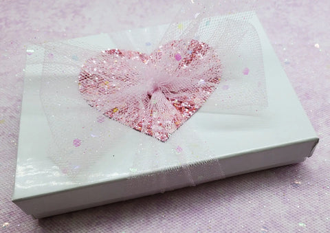 A white gift box with a pink glitter heart and sparkly tulle ribbon is perfect for presenting the Alexa Martha Designs Handmade Copper Teardrop Bangle. Displayed on a pale pink textured background.