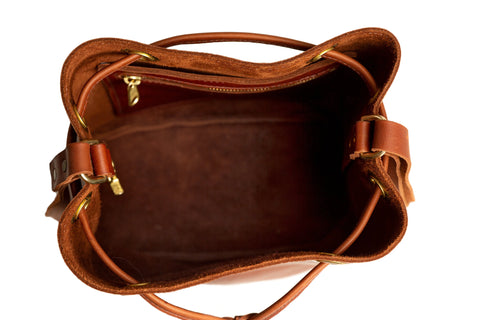 Top view of the Urban Southern Urban Bucket Bag, an open brown leather bag handcrafted in the USA, featuring gold hardware and an empty interior with a zippered side pocket.