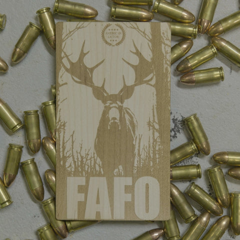 The American Lictor Wood Stickers feature a laser-etched deer and trees with “FAFO,” set on wood with durable 3M adhesive—ideal for fans of unique, engraved designs. Scattered brass bullets create a bold display on a gray surface.