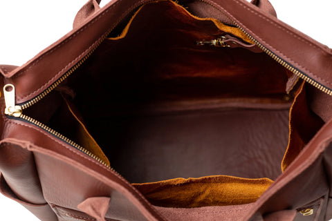 The Legacy Backpack Tote by Urban Southern features a gold zipper, spacious light brown-lined interior with an inner pocket, and convertible straps showcasing the brand’s signature heritage style. Bag shown empty.
