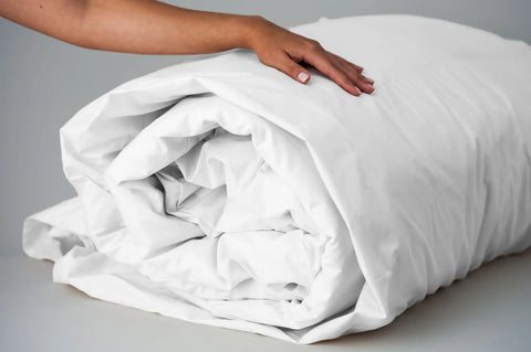 A hand gently rests on the neatly rolled Cotton Duvet Cover Set by American Blossom Linens, highlighting its quality construction and attention to detail against a neutral background.
