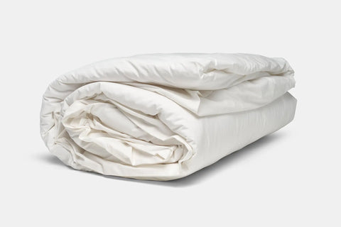 A neatly rolled-up Cotton Duvet Cover Set by American Blossom Linens rests on a light gray background, showcasing soft, plush fabric with clean folds that reflect the premium quality of this bedding.