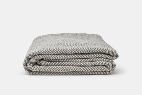 The Herringbone Weave Cotton Blanket by American Blossom Linens, in gray and white, is neatly folded on a light background—perfect for adding a cozy touch to any room.