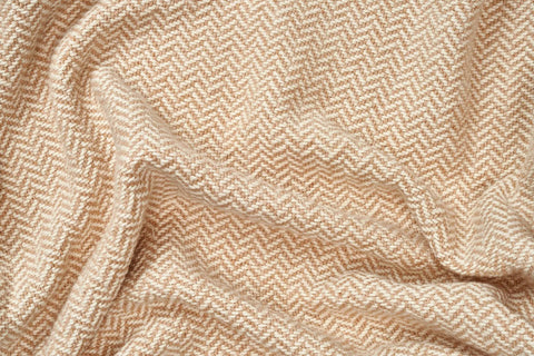 A close-up of the Herringbone Weave Cotton Blanket by American Blossom Linens shows its soft beige and white pattern with gentle folds, creating a cozy layer perfect for any space.