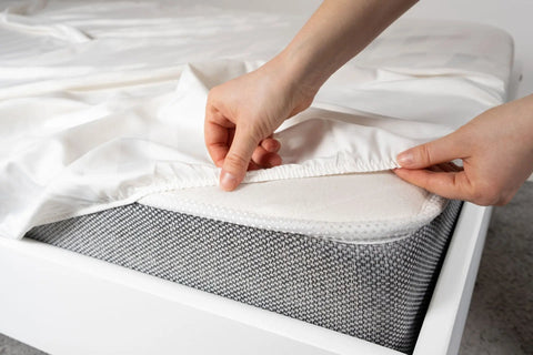 A person’s hands are shown spreading the American Blossom Linens Herringbone Weave Cotton Blanket over a grey mattress, adding a cozy touch to the bed.