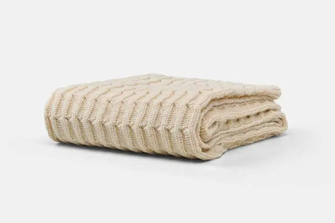 The American Blossom Linens Cotton Knitted Baby Blanket is a cream-colored, cable-knit blanket, ideal for a crib or stroller, shown folded against a plain white background.