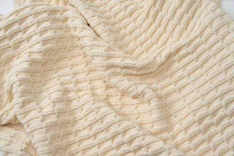 A close-up of the Cotton Knitted Baby Blanket by American Blossom Linens shows its cream color and textured ribbed pattern—soft, cozy, and ideal for draping in a crib or stroller.