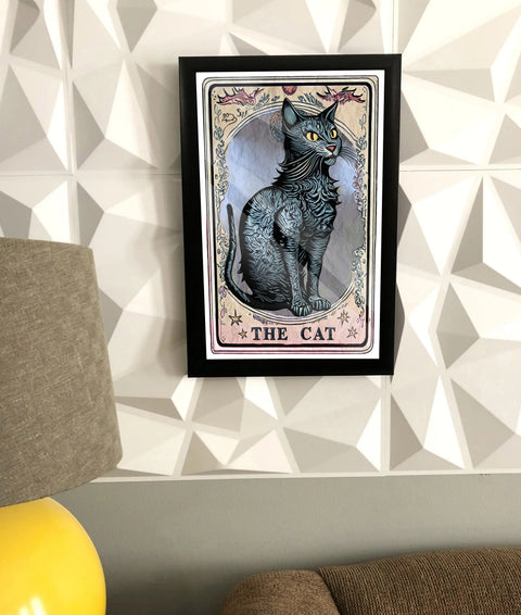 The NEW Poster, “Terot Card” by Skinny Petes Gourmet Catnip features a mystical black cat and ornate designs, displayed framed on a geometric-patterned wall above a gray couch with a lamp partially visible on the left.