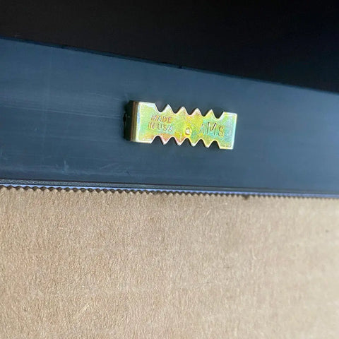 Close-up of a brass hanger stamped MADE IN USA and AWS, attached to the back of a Skinny Petes Gourmet Catnip art frame for the NEW Poster, “Terot Card”. The frame edge is black; backing is light brown.