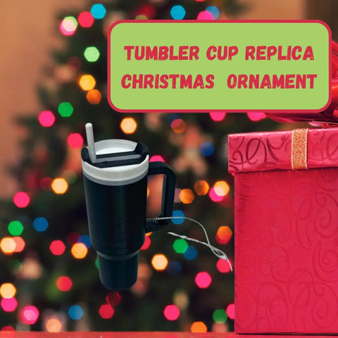 A Tumbler Cup Replica Christmas Ornament by Chatelet Manufacturing hangs before a festive tree and red gift box—ideal for unique holiday décor. Text: “TUMBLER CUP REPLICA CHRISTMAS ORNAMENT.” Made in USA, 2023’s popular water bottle replica mug ornament.