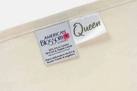 Close-up of a fabric tag reading American Blossom Linens, Queen, showing details about the Cotton Single [Separate] Flat Bed Sheet, made from 55% U.S.A. cotton and 45% organic cotton, proudly crafted in the U.S.A.