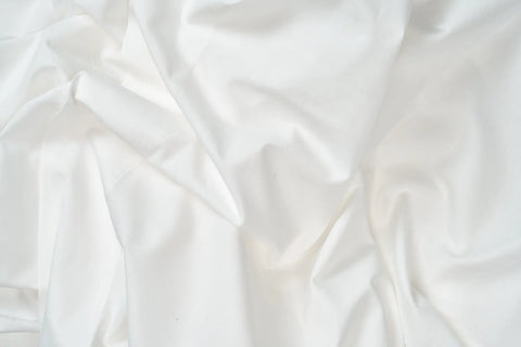 A close-up of the Cotton Percale Bed Sheet Set by American Blossom Linens shows smooth, white folds and gentle creases, crafted from the finest USA grown cotton for a clean, subtly textured look.
