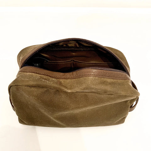 The Rogue Industries Waxed Canvas Dopp Kit, in brown with a zipper, sits on a plain white surface—partially open to show its roomy interior and inner pocket.