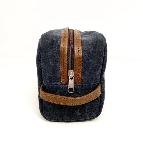 The Rogue Industries Waxed Canvas Dopp Kit is a small, dark blue bag with brown leather accents and zipper closure, shown upright against a plain white background.