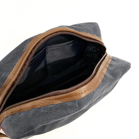 The Rogue Industries Waxed Canvas Dopp Kit in dark gray features a brown leather zipper trim and an empty black interior pocket, displayed open against a white background.